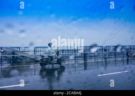 Une personne passant par le 2ème pont Hoogly sur un scooter sous la pluie, image de mousson de Kolkata, Bengale-Occidental, Inde. Banque D'Images