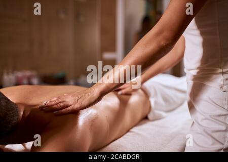Les mains de femmes douces avec une belle manucure de masseuse professionnelle, faisant massage de relaxation du corps à la cliente masculine, centre de beauté santé de bien-être conce Banque D'Images