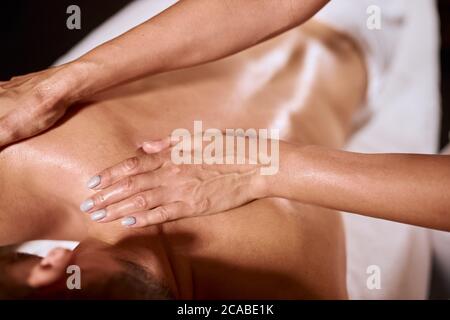 Gros plan des mains des femmes effectuant un massage aromatique sur le dos des hommes, masseur professionnel gardant les paumes sur l'épaule du jeune client, concept spa santé beauté Banque D'Images
