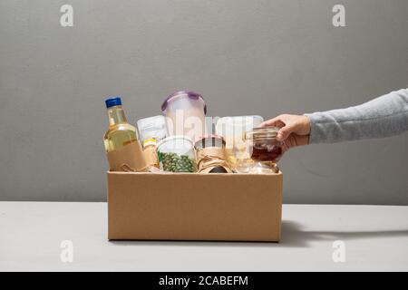 Portez un volontaire en portant des gants contenant des aliments dans une boîte en carton contenant divers aliments. Banque D'Images