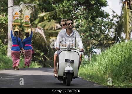 Asie, Indonésie, Bali, jeune couple caucasien, portant des vêtements élégants et décontractés, en appréciant une promenade sur un Vespa classique à travers le paysage balinais typique, pa Banque D'Images