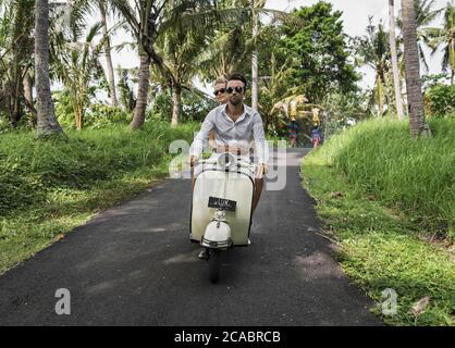 Asie, Indonésie, Bali, jeune couple caucasien, portant des vêtements élégants et décontractés, en appréciant une promenade sur un Vespa classique à travers le paysage balinais typique, pa Banque D'Images