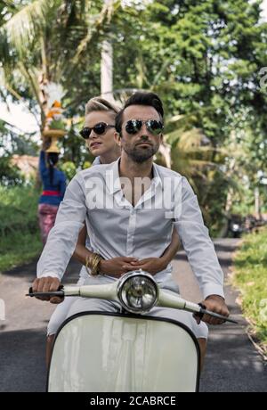 Asie, Indonésie, Bali, jeune couple caucasien, portant des vêtements élégants et décontractés, en appréciant une promenade sur un Vespa classique à travers le paysage balinais typique, pa Banque D'Images