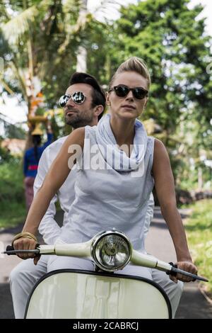 Asie, Indonésie, Bali, jeune couple caucasien, portant des vêtements élégants et décontractés, en appréciant une promenade sur un Vespa classique à travers le paysage balinais typique, pa Banque D'Images