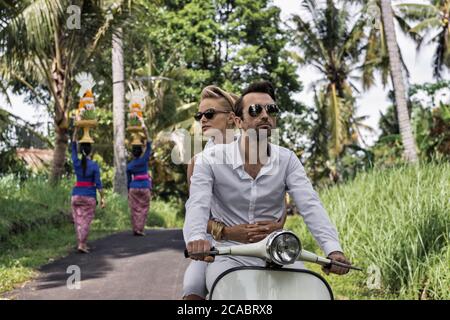 Asie, Indonésie, Bali, jeune couple caucasien, portant des vêtements élégants et décontractés, en appréciant une promenade sur un Vespa classique à travers le paysage balinais typique, pa Banque D'Images