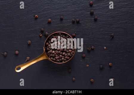 Food Spices concept vue de dessus du poivre noir biologique en cuivre sur pierre d'ardoise noire avec espace de copie Banque D'Images