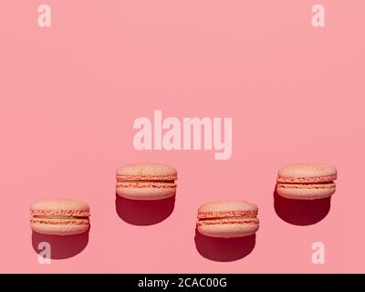 Macarons roses avec espace de copie. Rangée de macarons ou macarons français parfaits sur fond rose. Vue de dessus ou plat. Lumière dure Banque D'Images