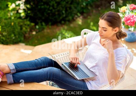 Prise de vue en grand angle d'une femme confiante utilisant un ordinateur portable tout en étant assise sur un balcon à la maison. Bureau à domicile. Banque D'Images