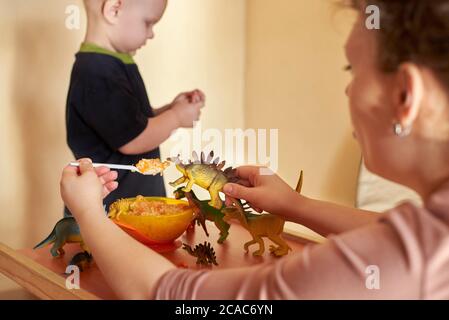 Maman nourrit les dinosaures de jouet à partir d'une cuillère, maman joue avec son fils. Banque D'Images