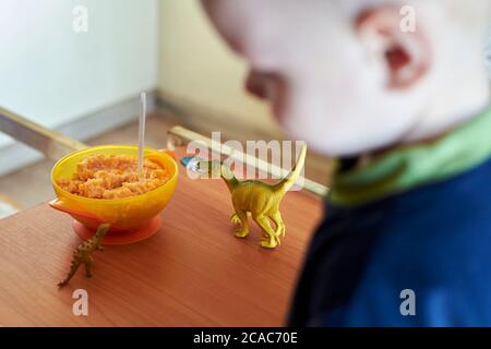 Les dinosaures jouets sont placés sur une table pour enfants près d'une assiette de porridge avec une cuillère. Banque D'Images