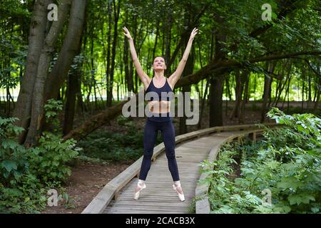 belle fille ballerina à pointe chaussures fait des exercices sur un chemin en bois dans un parc forestier. concept d'entraînement en plein air sûr Banque D'Images