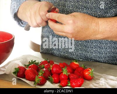 Gros plan sur les mains d'un homme coupant des fraises. Un homme prépare un dessert rafraîchissant aux fraises pour ses invités dans la cuisine Banque D'Images