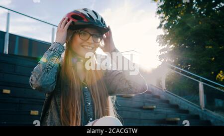 Portrait d'une jeune femme en train de régler l'équipement de sécurité, un casque tout en étant assis sur les escaliers du skate Park. Photo de haute qualité Banque D'Images