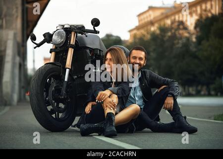 Un beau couple de motards amoureux est assis sur la route à côté des motos dans la ville Banque D'Images