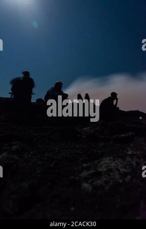 Silhouettes de personnes assises au bord du cratère du volcan Erta Ale, en Éthiopie, en pleine lune Banque D'Images