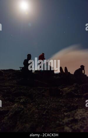 Silhouettes de personnes assises au bord du cratère du volcan Erta Ale, en Éthiopie, en pleine lune Banque D'Images
