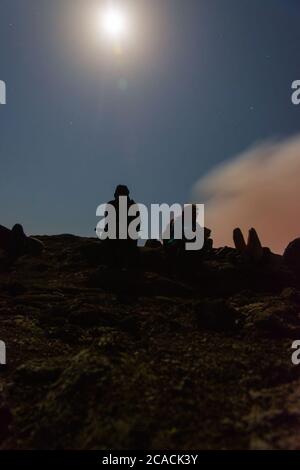 Silhouettes de personnes assises au bord du cratère du volcan Erta Ale, en Éthiopie, en pleine lune Banque D'Images