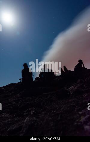 Silhouettes de personnes assises au bord du cratère du volcan Erta Ale, en Éthiopie, en pleine lune Banque D'Images