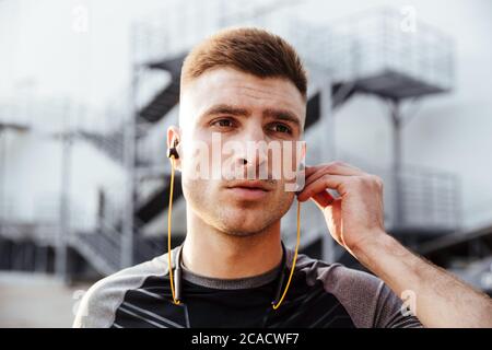 Image d'un sportif caucasien non rasé utilisant des écouteurs tout en travaillant en zone urbaine à l'extérieur Banque D'Images