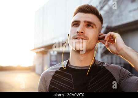 Image d'un sportif heureux utilisant des écouteurs lors de l'entraînement en zone urbaine à l'extérieur Banque D'Images