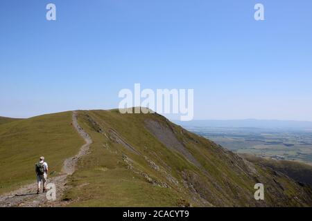 Walker sur le sentier le long du sommet de Blencathra en regardant vers Hallsfell Top avec des gens sur la ligne d'horizon au sommet, English Lake District, Cumbria, Royaume-Uni. Banque D'Images