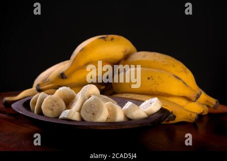 Un bouquet de bananes et une banane tranché dans un bol sur une table Banque D'Images