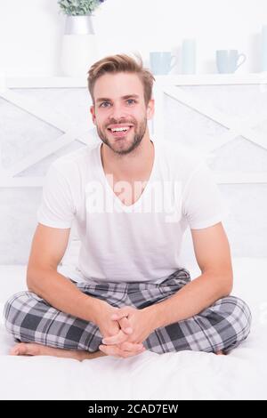 Bonjour. Guy heureux s'asseoir sur le lit. Hipster homme dans matin. Endormi et éveillé. Détendez-vous à l'aise. Smiling guy porter des pyjamas à la maison. Cheerful énergie positive. Bel homme profiter de sa matinée parfaite. Banque D'Images