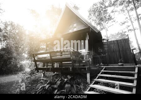 Maison thaïlandaise en bois dur sur le côté de la rivière en noir et blanc avec lumière du soleil et lumière de la lumière du soleil. Le style unique de toit haut est adapté aux tropiques Banque D'Images