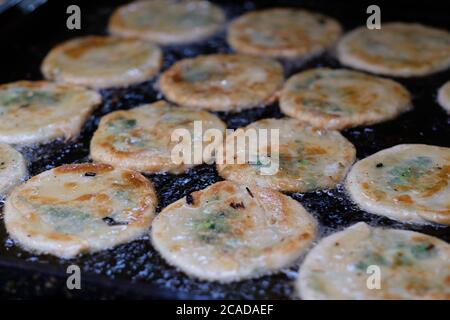 fermez le groupe de pancakes frits à l'oignon dans une casserole noire. Huile bouillante. La cuisine populaire traditionnelle chinoise. Défoqué Banque D'Images