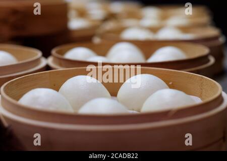 Gros plan des petits pains à grains blancs dans le cuiseur vapeur. Dim sum chinois traditionnel. Arrière-plan de perspective flou Banque D'Images