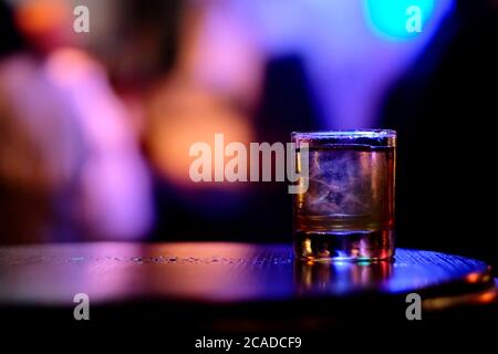 gros plan sur un verre de cocktail sur une table de bar en bois. Arrière-plan flou de lumières colorées Banque D'Images