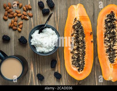 Petit déjeuner sur une table en bois : fromage cottage dans un bol, papaye en deux, amandes et mûres. Banque D'Images