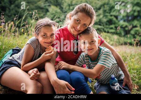 Portrait d'une mère souriante et de ses deux enfants adorables, assis sur un sentier qui fait une pause dans leur randonnée en famille Banque D'Images