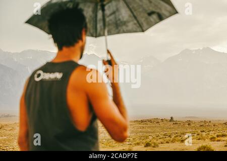 Jeune homme dans le désert du nord de la Californie, tenant un parapluie sous la pluie. Banque D'Images