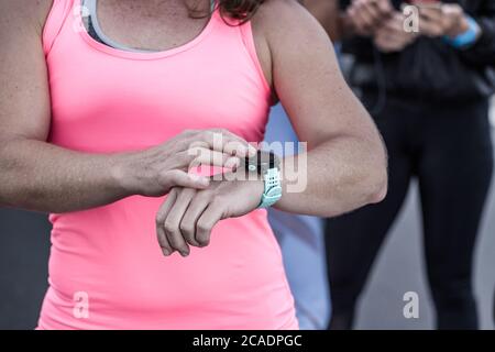 Une sportswoman non reconnaissable en haut rose contrôle de l'impulsion sur la montre intelligente pendant l'entraînement en plein air Banque D'Images