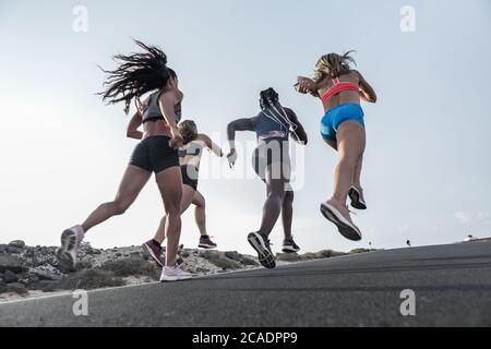 Des amies anonymes multiethniques dans sportswear sprinting sur la route asphaltée contre le ciel nocturne sans nuages pendant la séance de course à pied en périphérie Banque D'Images