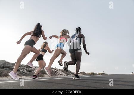 Vue arrière de sportswomen multiracial anonyme qui se lance sur la route asphaltée contre le ciel du soir pendant l'entraînement en plein air en périphérie Banque D'Images