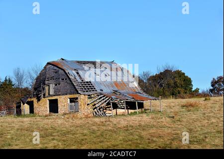 La grange en pierre abandonnée est en ruines. La structure supérieure en bois est en cours de spéléologie et une partie de l'étain sur le toit a sauté. Banque D'Images