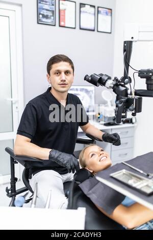 Nous améliorons votre sourire. Dentiste masculin observez le patient à l'aide d'un microscope binoculaire dentaire professionnel. Banque D'Images