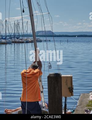 Steinhude, Allemagne, 29 mai 2020 : l'homme en chemise rouge aligne le mât de son bateau à voile pour le voyage sur le Steinhuder Meer près de Hanovre. Banque D'Images