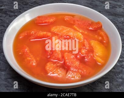 Gros plan de tranches de pamplemousse rouge rubis en conserve, non sucrée, avec du jus naturel, dans un bol en céramique gris/gris, sur une surface en granit. Banque D'Images