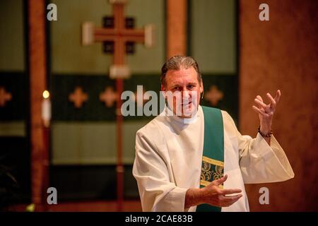 Portant une robe blanche, un diacre enthousiaste prêche un sermon dans la chaire d'une église catholique du sud de la Californie. Banque D'Images