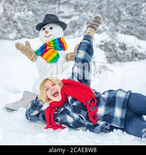 Bonhomme de neige et fille drôle en hiver dehors. Charmant bonhomme de neige dans un village enneigé. Banque D'Images