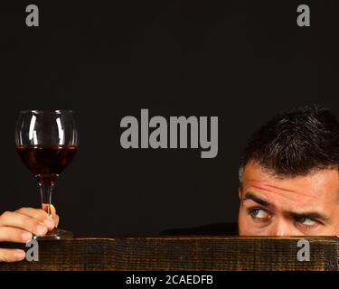 Degustator avec face cachée derrière une chaise en bois. Le sommelier goûte des boissons chères. Concept de dégustation de vins et de dégustation. Homme avec barbe tient un verre de vin sur fond marron foncé, espace de copie Banque D'Images