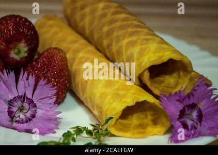 Tubes à gaufres, fraises et fleurs de la carnation . Composition sur un fond en bois clair décoré de fleurs de carnation Banque D'Images
