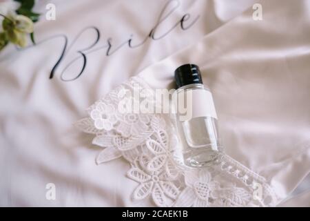 Flacon de parfum avec capuchon noir sur tissu blanc avec dentelle et lettrage BRIDE. Banque D'Images