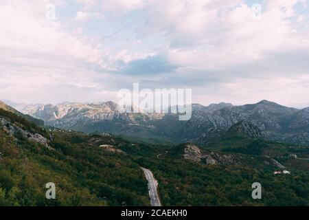 Une route de montagne en serpentin au milieu d'une forêt verte avec vue sur les montagnes et le ciel couvert de nuages. Banque D'Images