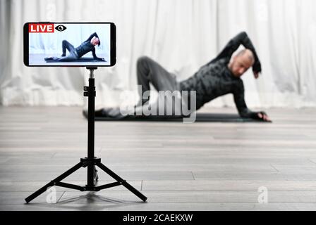 Homme avec haltères de gym et équilibre. Exercices d'entraînement en direct sur smartphone pour suivre sportif sur les médias sociaux. Coronavirus ou quarantaine Covid-19. Banque D'Images