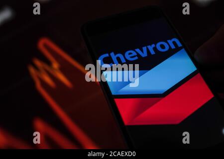Sur cette photo, un logo Chevron Corporation apparaît sur un smartphone, sur un fond de graphique boursier. Banque D'Images