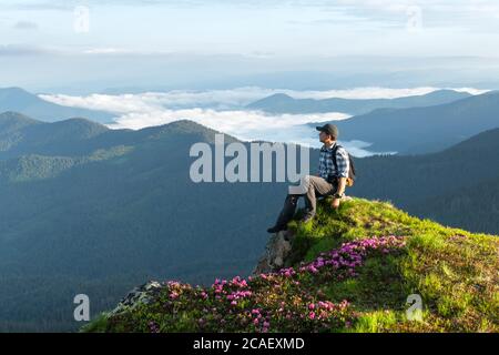 Un touriste se trouve au bord d'une falaise couverte d'un tapis rose de fleurs de rhododendron en été. Montagnes brumeuses en arrière-plan. Photographie de paysage Banque D'Images